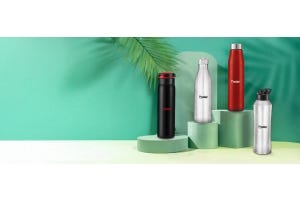 Four Prestige stainless steel water bottles in black, silver, and red colors displayed on green podiums against a tropical-themed green background.