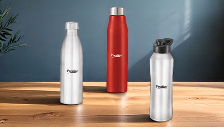 Four Prestige stainless steel water bottles in black, silver, and red colors displayed on green podiums against a tropical-themed green background.