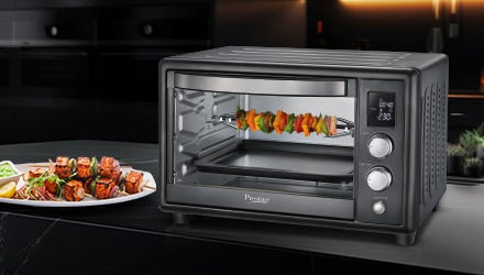 Prestige OTG oven grilling vegetables and meats with a plate of grilled food on a modern kitchen countertop.